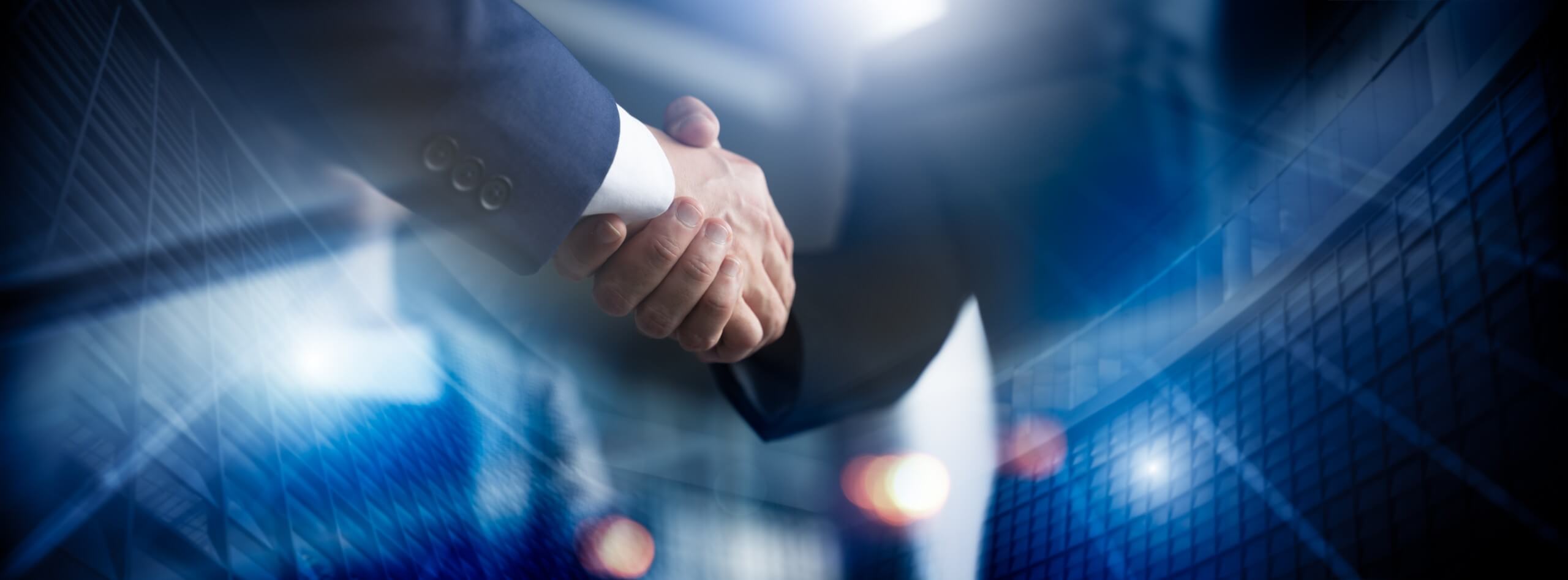 Business professionals shaking hands in front of modern office buildings, symbolizing partnership.