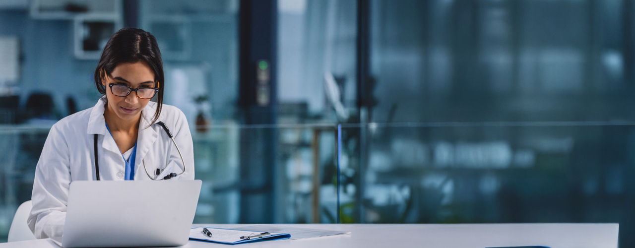 Person using a laptop device dressed in medical professional clothing.